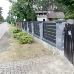 Nowoczesne ogrodzenie panelowe z betonowymi słupkami i czarną furtką z numerem 40, widok z chodnika na tle ulicy i domu.