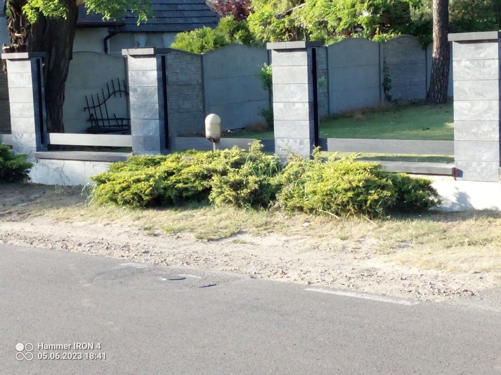 Nowoczesne ogrodzenie panelowe z elementami kamiennymi w Żarkach, widok z poziomu ulicy, z przodu krzewy.