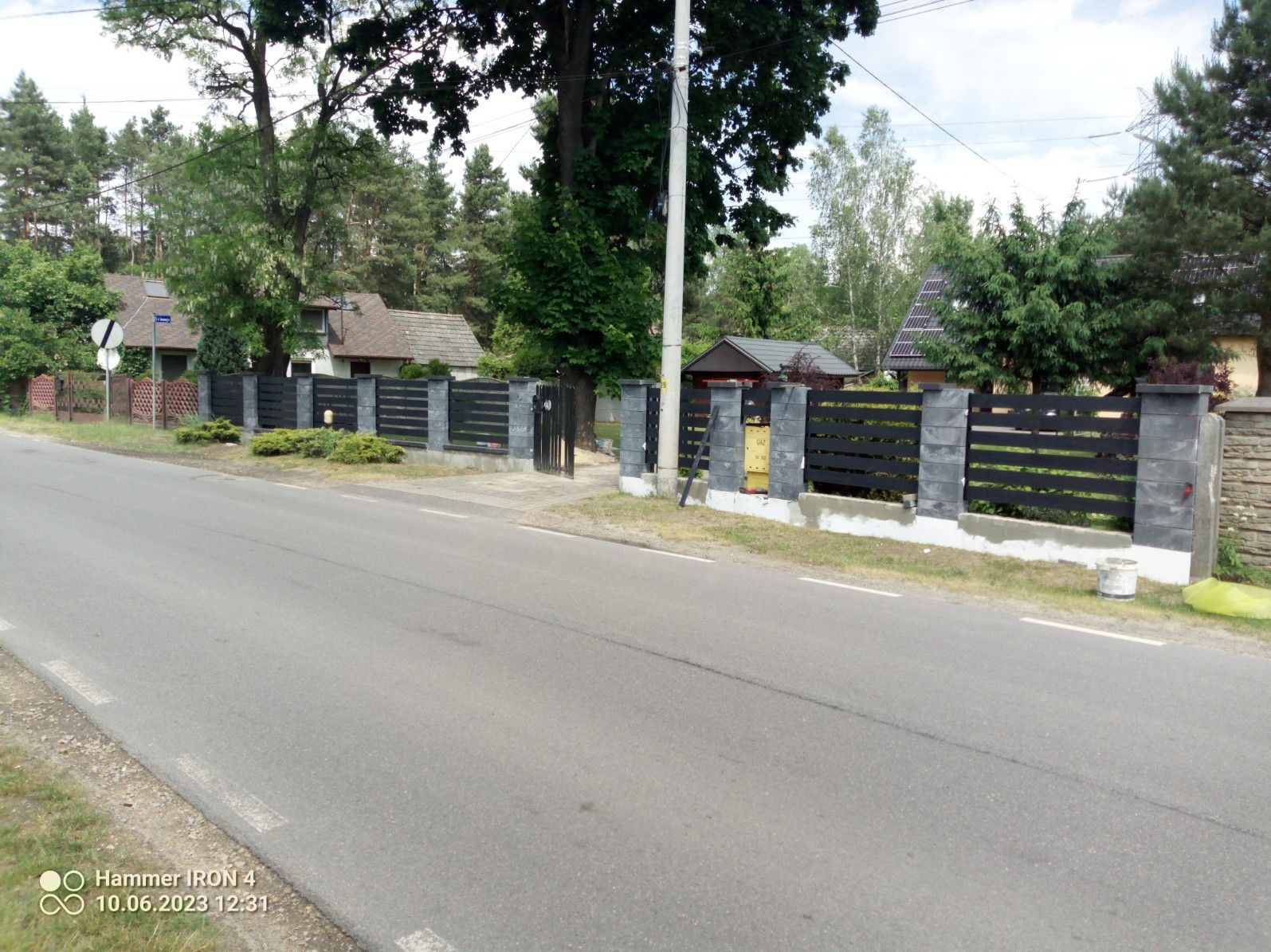 Nowoczesne, poziome ogrodzenie z czarnych desek i szarych betonowych słupków, widok z ulicy, z żółtą skrzynką gazową przy jednym ze słupków.