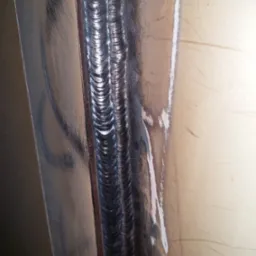 Szczegółowe zbliżenie na potrójny spaw na metalowej konstrukcji, widoczne regularne ślady po spawaniu i lekkie zarysowania na powierzchni metalu.