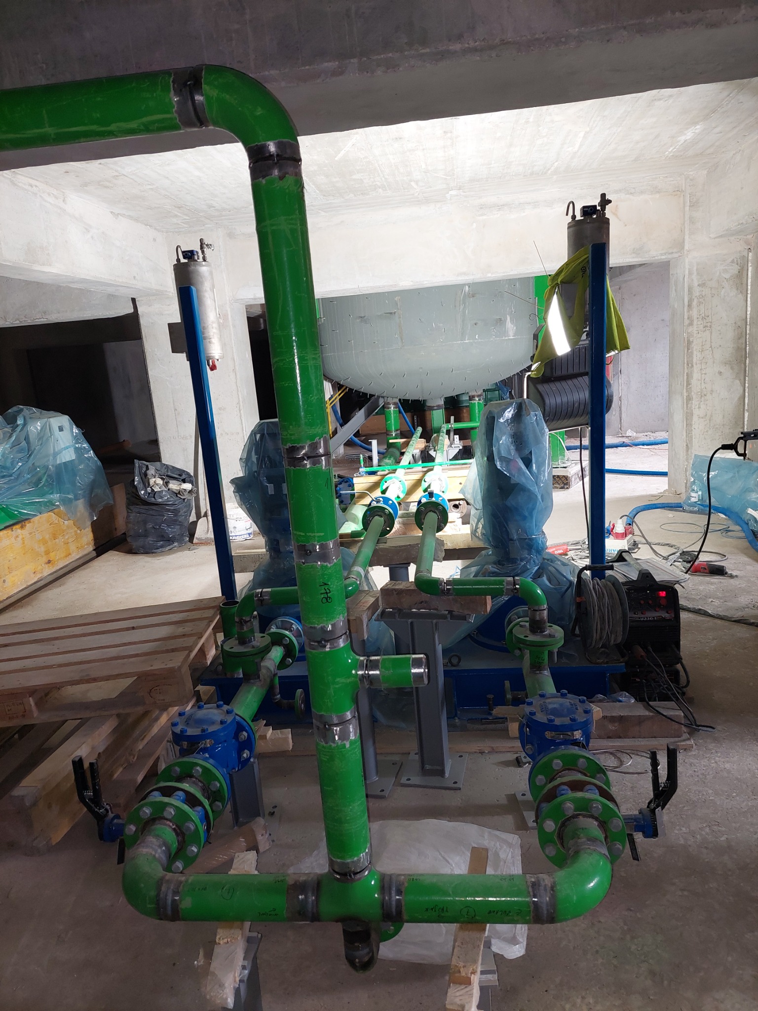 Instalacja przemysłowa z zielonych rur, spawana na budowie, z widocznym spawarką i elementami podłączeniowymi