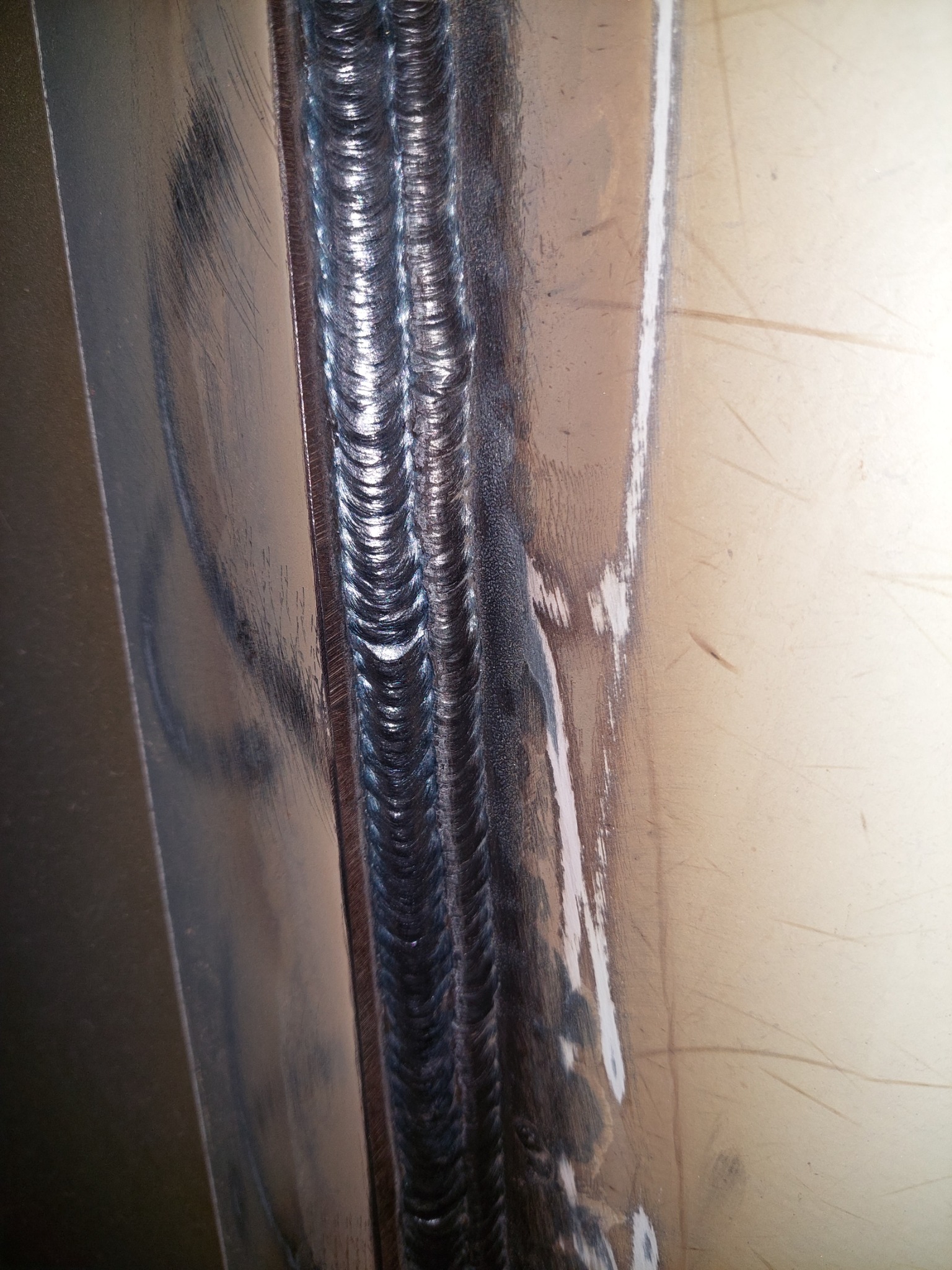 Szczegółowe zbliżenie na potrójny spaw na metalowej konstrukcji, widoczne regularne ślady po spawaniu i lekkie zarysowania na powierzchni metalu.