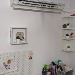 artermo.pl Arkadiusz Klukowski - Biała klimatyzacja Panasonic zamontowana na ścianie w pokoju. Pod spodem biurko z różnymi przedmiotami i dekoracjami. Ujęcie z dołu, widoczne elementy wyposażenia wnętrza.