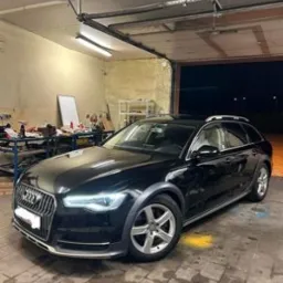 Czarny samochód Audi Allroad zaparkowany w garażu z widocznym warsztatem w tle.