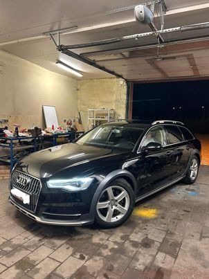 Czarny samochód Audi Allroad zaparkowany w garażu z widocznym warsztatem w tle.