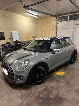Szary Mini Cooper z czarnymi felgami i pasami na masce oraz dachu z motywem Union Jack, stojący w warsztacie z widocznymi narzędziami w tle.