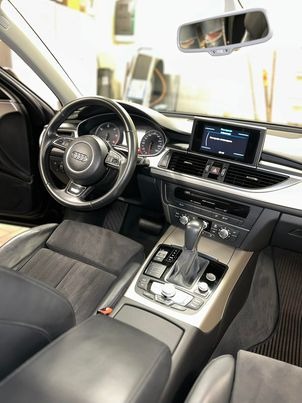 Wnętrze czarnego Audi A6 z widocznymi elementami deski rozdzielczej, kierownicy z logo marki i automatycznej skrzyni biegów po praniu tapicerki.