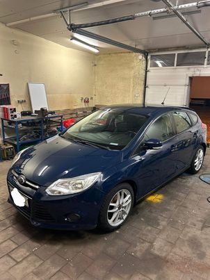 Niebieski Ford Focus po umyciu, stojący w garażu z podniesioną bramą, widoczne ślady wody na podłodze.