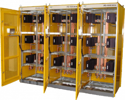 Żółta szafa elektryczna z otwartymi drzwiami, widoczne miedziane szyny i czarne moduły elektroniczne, trzy segmenty z identycznym układem.