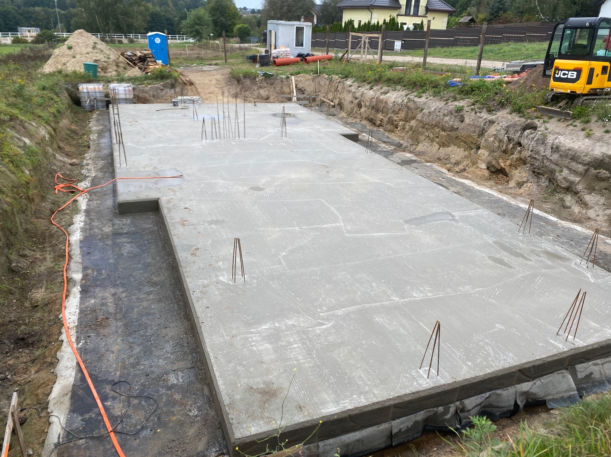 Wylany fundament z wystającymi prętami zbrojeniowymi na budowie w Kowalach, widoczna izolacja przeciwwilgociowa i wykopane ściany fundamentowe.