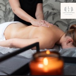 Shchetinina Larysa - Kobieta podczas masażu pleców w salonie, widoczna zapalona świeca i logo salonu na ścianie.