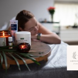 Shchetinina Larysa - Relaksujący masaż: kobieta leży na stole, a na drewnianym stoliku obok płonie świeca zapachowa, olejek eteryczny, krem i masło do ciała, tworząc atmosferę spa.