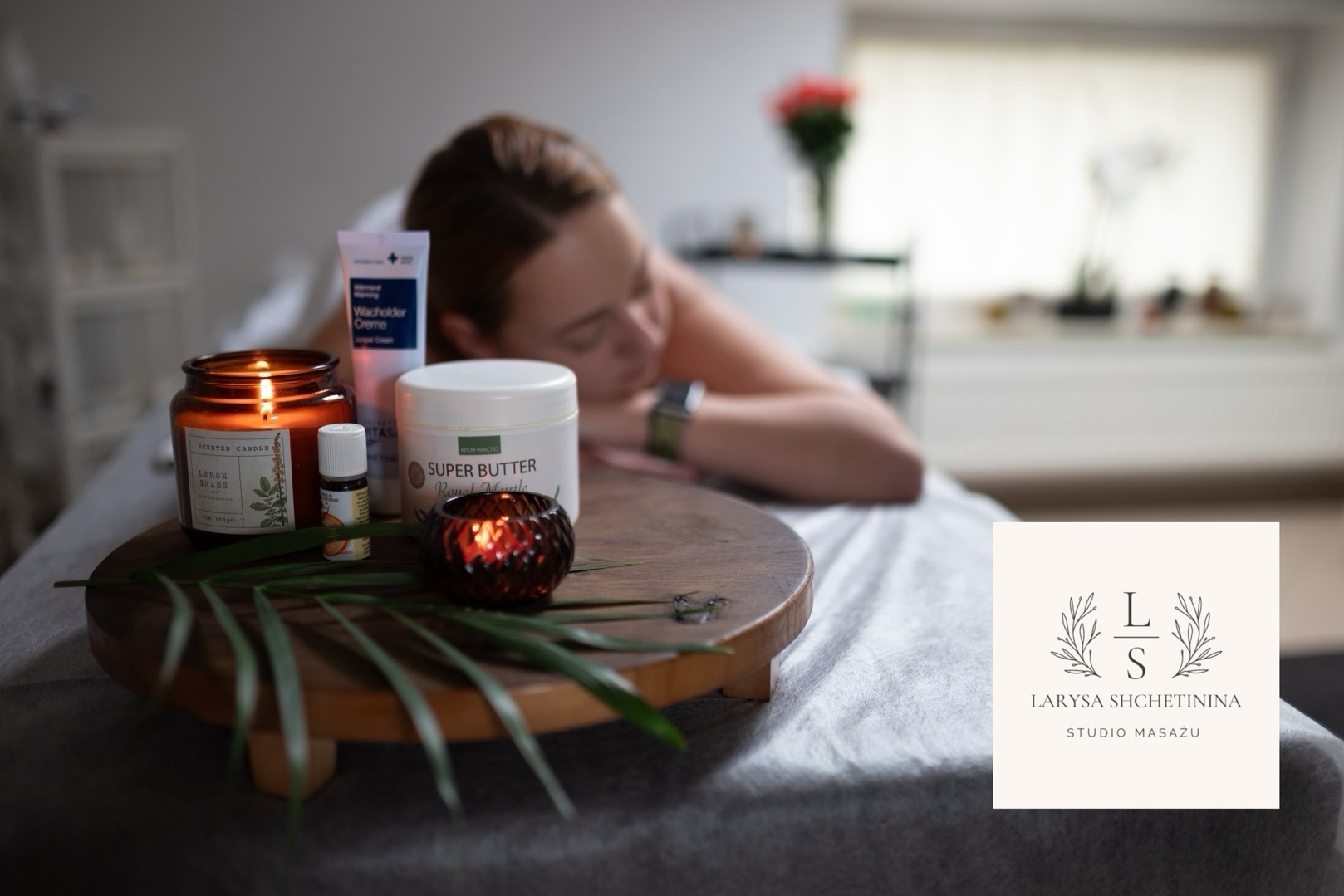 Relaksujący masaż: kobieta leży na stole, a na drewnianym stoliku obok płonie świeca zapachowa, olejek eteryczny, krem i masło do ciała, tworząc atmosferę spa.