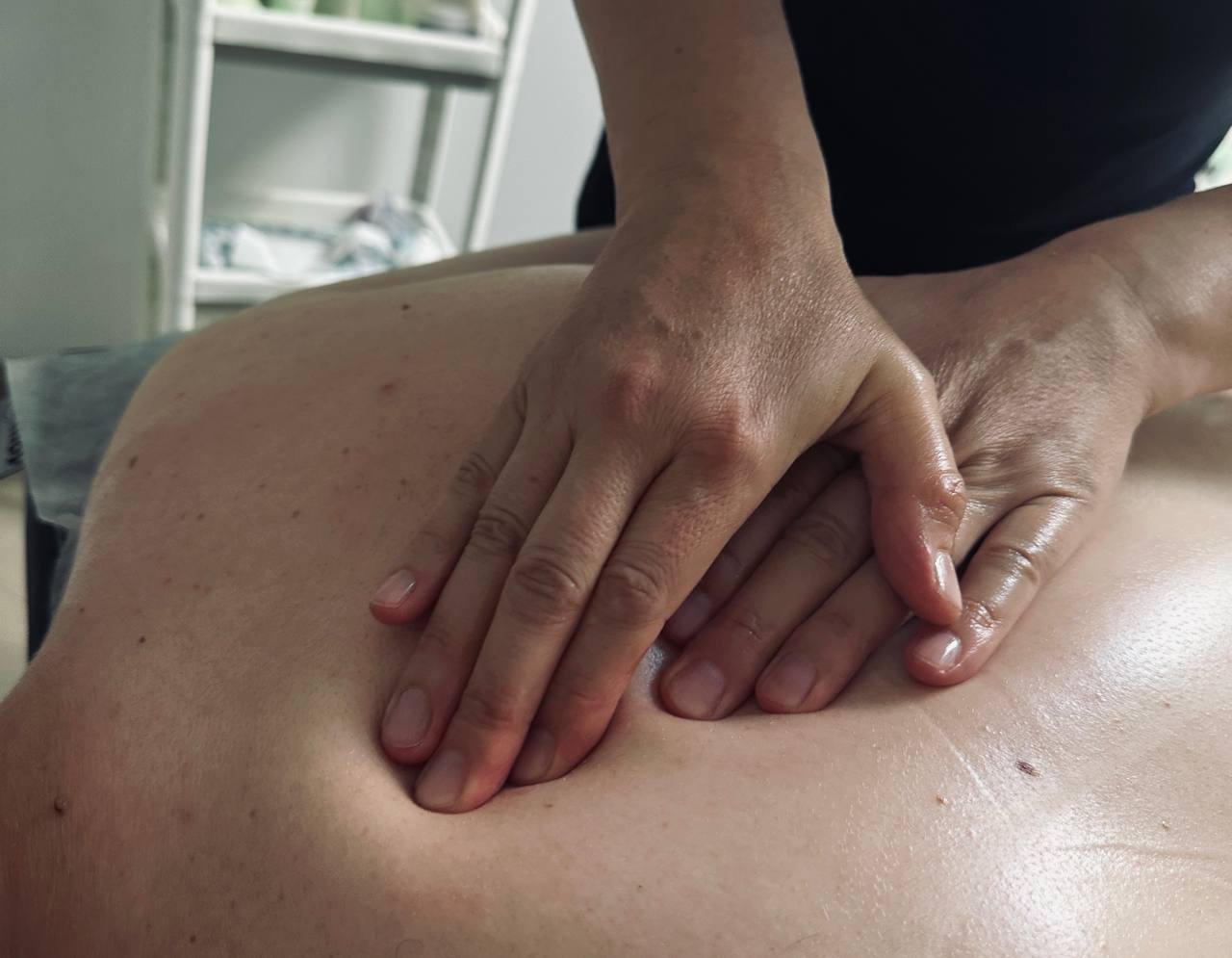 Dłonie masujące plecy klienta, widoczne drobne znamiona na skórze, z bliska, w gabinecie. Dłonie pokryte olejkiem do masażu.