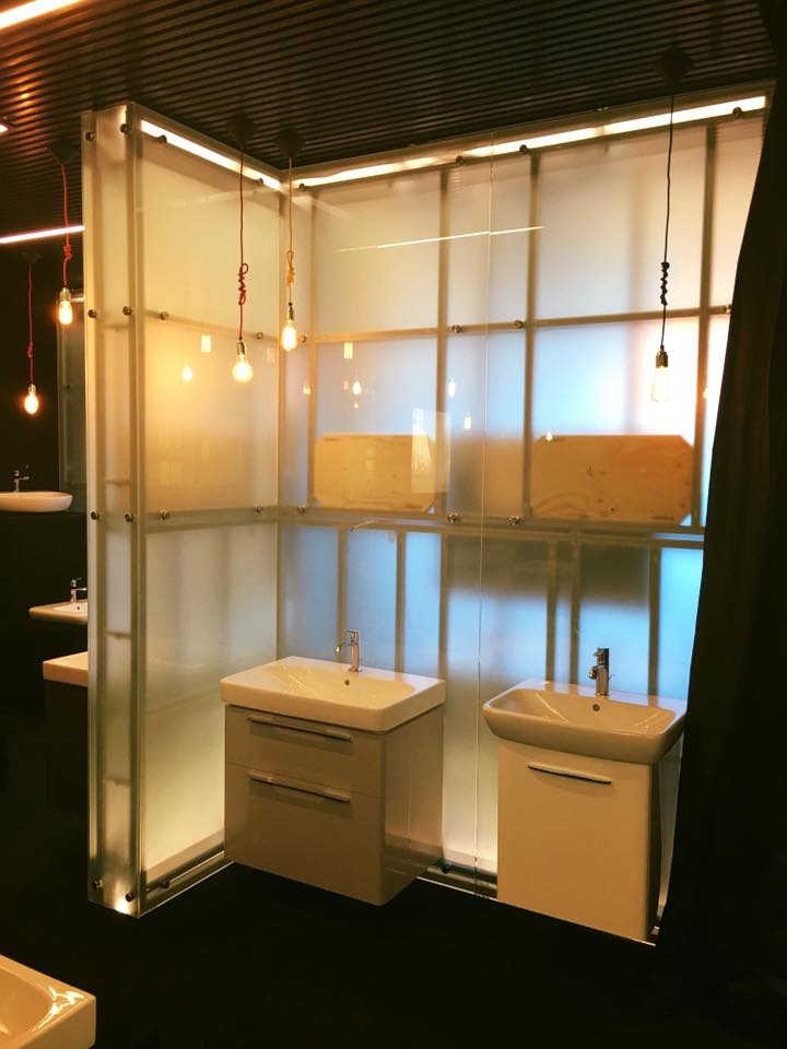 Nowoczesna aranżacja łazienki z umywalkami na szafkach, oświetleniem dekoracyjnym i ścianką z mlecznego szkła. Minimalistyczny design z wiszącymi żarówkami.