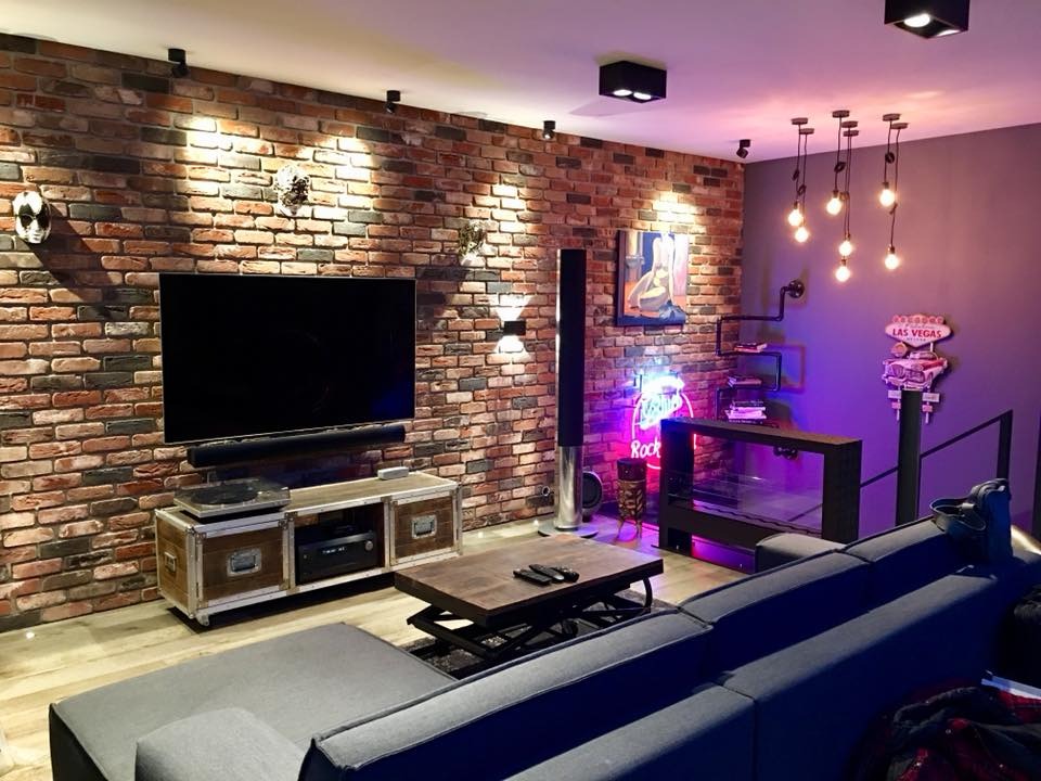 Loftowy salon z ceglaną ścianą, oświetleniem punktowym i neonem 'Rock'. Nowoczesny design z szarą sofą i elementami dekoracyjnymi. Klimatyczne wnętrze.