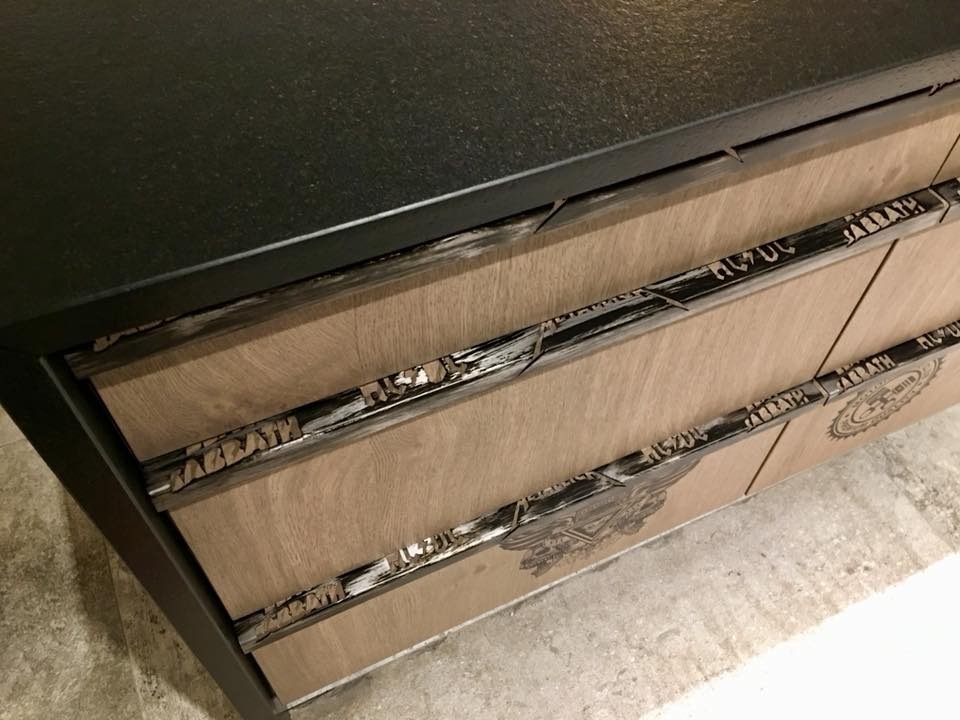 Stylowa komoda z trzema szufladami, drewniane fronty z metalowymi uchwytami z napisami 'AC/DC' i 'SABBATH', czarny blat, industrialny design.