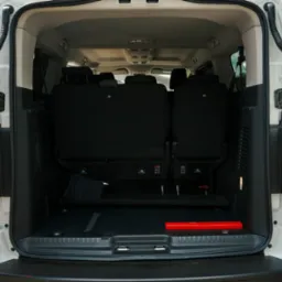 Otwarty bagażnik białego busa z widocznymi siedzeniami pasażerskimi i trójkątem ostrzegawczym.