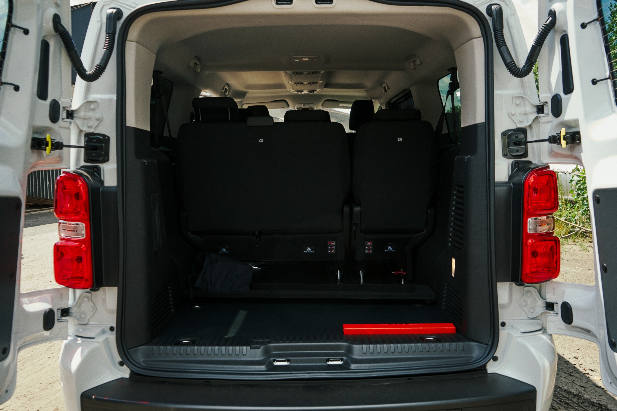 Otwarty bagażnik białego busa z widocznymi siedzeniami pasażerskimi i trójkątem ostrzegawczym.