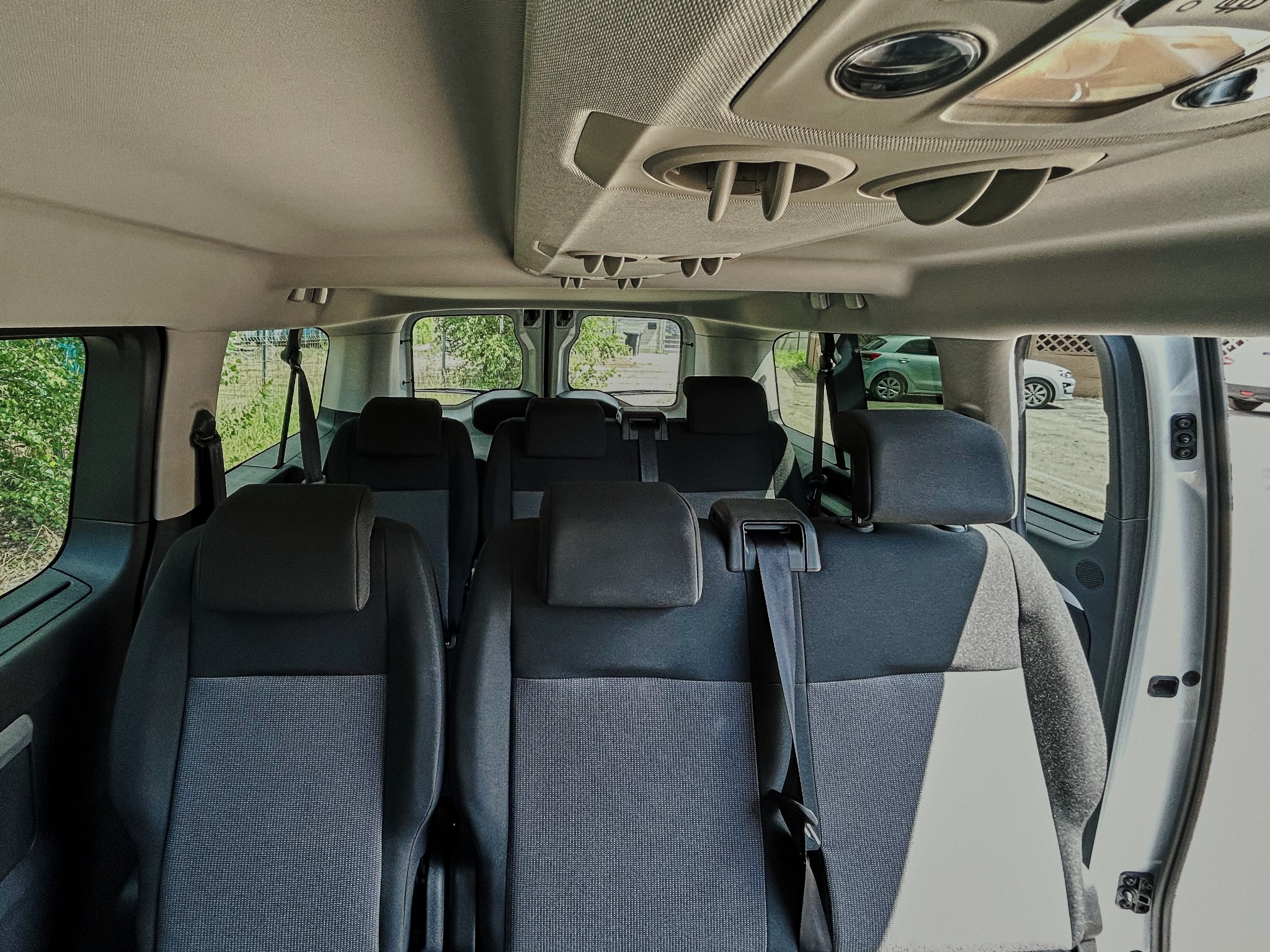 Wnętrze busa z trzema rzędami siedzeń, widok od tyłu, z detalami systemu wentylacji sufitowej.