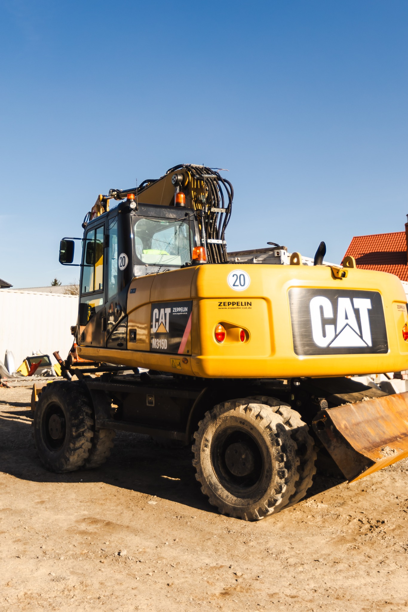Żółta koparka kołowa CAT M315D na placu budowy z widocznym łyżką i oznaczeniami Zeppelin, na tle błękitnego nieba.