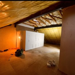 eR-Ka KAROL WOŹNICKI - Adaptacja poddasza: izolacja pianą, zabudowa ścianek działowych, widoczne narzędzia i materiały budowlane w surowym wnętrzu.