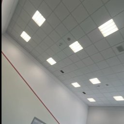 eR-Ka KAROL WOŹNICKI - Wnętrze po remoncie: białe ściany z czerwoną linią, sufit z kwadratowymi lampami, szklana balustrada i okno. Widok z dołu, ukośny kadr.