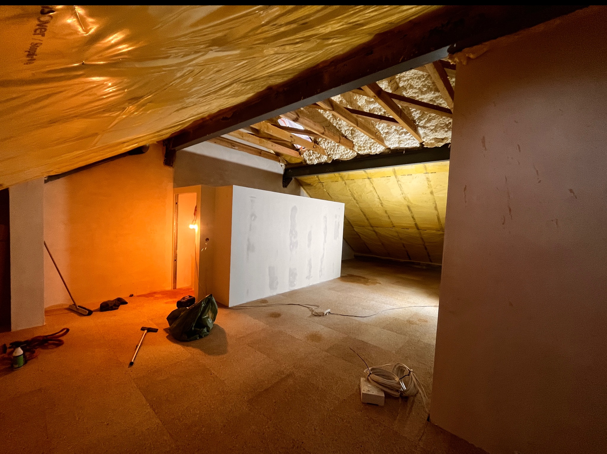 Adaptacja poddasza: izolacja pianą, zabudowa ścianek działowych, widoczne narzędzia i materiały budowlane w surowym wnętrzu.