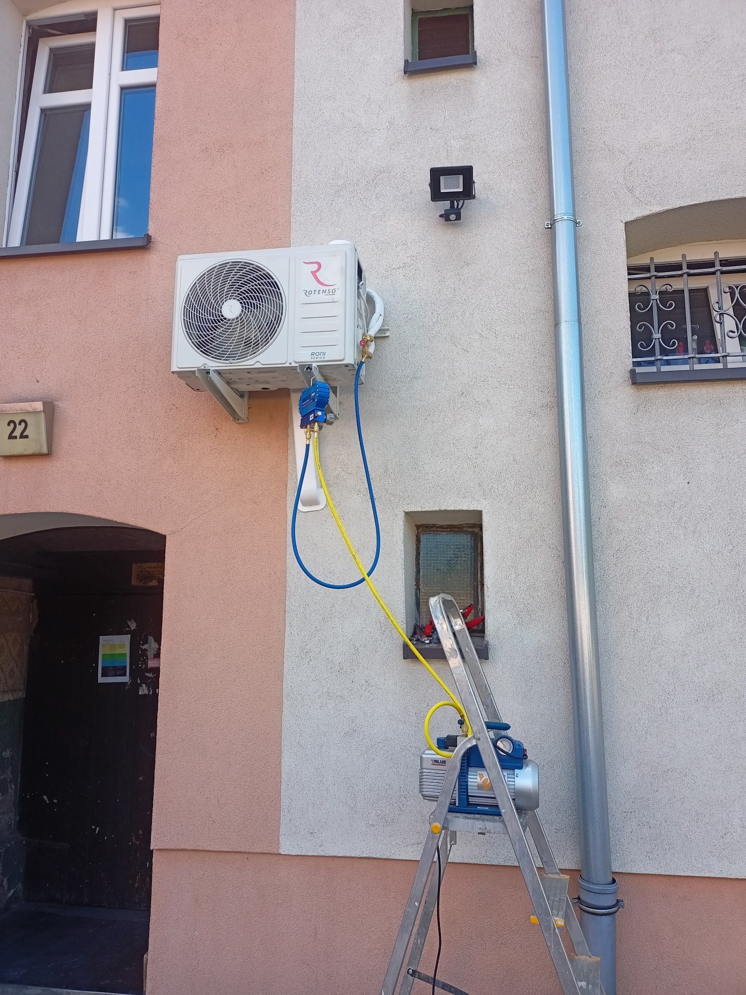 Montaż klimatyzacji Rotenso na elewacji budynku, widoczna pompa próżniowa Value na drabinie i podłączone przewody serwisowe.