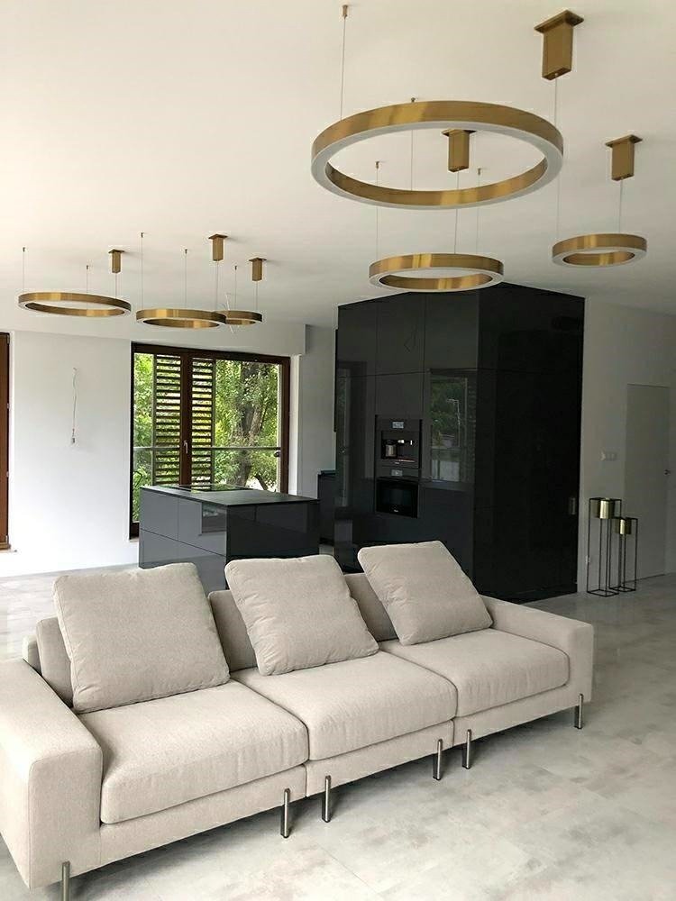 Nowoczesny salon z beżową sofą i okrągłymi złotymi lampami wiszącymi, czarna zabudowa kuchenna w tle.