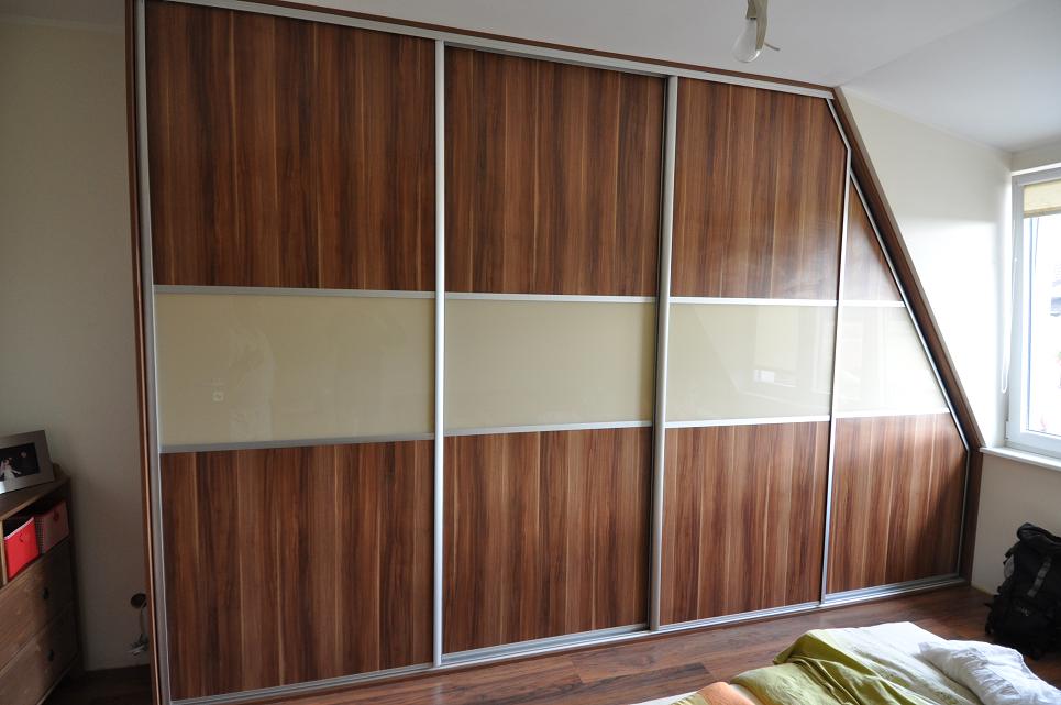 Duża, brązowa szafa przesuwna z drewnopodobnymi panelami i mlecznymi szybami, dopasowana do skosu dachu w pokoju.