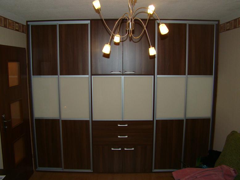 Duża, brązowo-beżowa szafa przesuwna z szufladami, oświetlona ozdobnym żyrandolem.