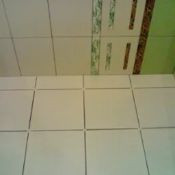 Świeżo ułożone, jasne płytki podłogowe z krzyżykami dystansowymi, widoczne fragmenty dekoracyjnych płytek ściennych z motywami roślinnymi w odcieniach zieleni i brązu.