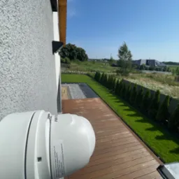 Kamera monitoringu Hikvision zamontowana na elewacji domu w Oławie, z widokiem na drewniany taras i zadbany ogr&oacute;d.
