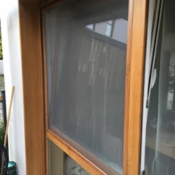 Zamknięta moskitiera w drewnianej ramie okiennej, widok z zewnątrz na balkon.