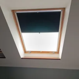 Ciemna, plisowana przesłona okienna w drewnianej ramie okna dachowego, częściowo zasłonięta, widok z dołu.