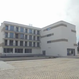 Nowoczesny budynek wielorodzinny z balkonami i elementami dekoracyjnymi na elewacji, widok z poziomu gruntu. Zewnętrzne prace wykończeniowe w toku.