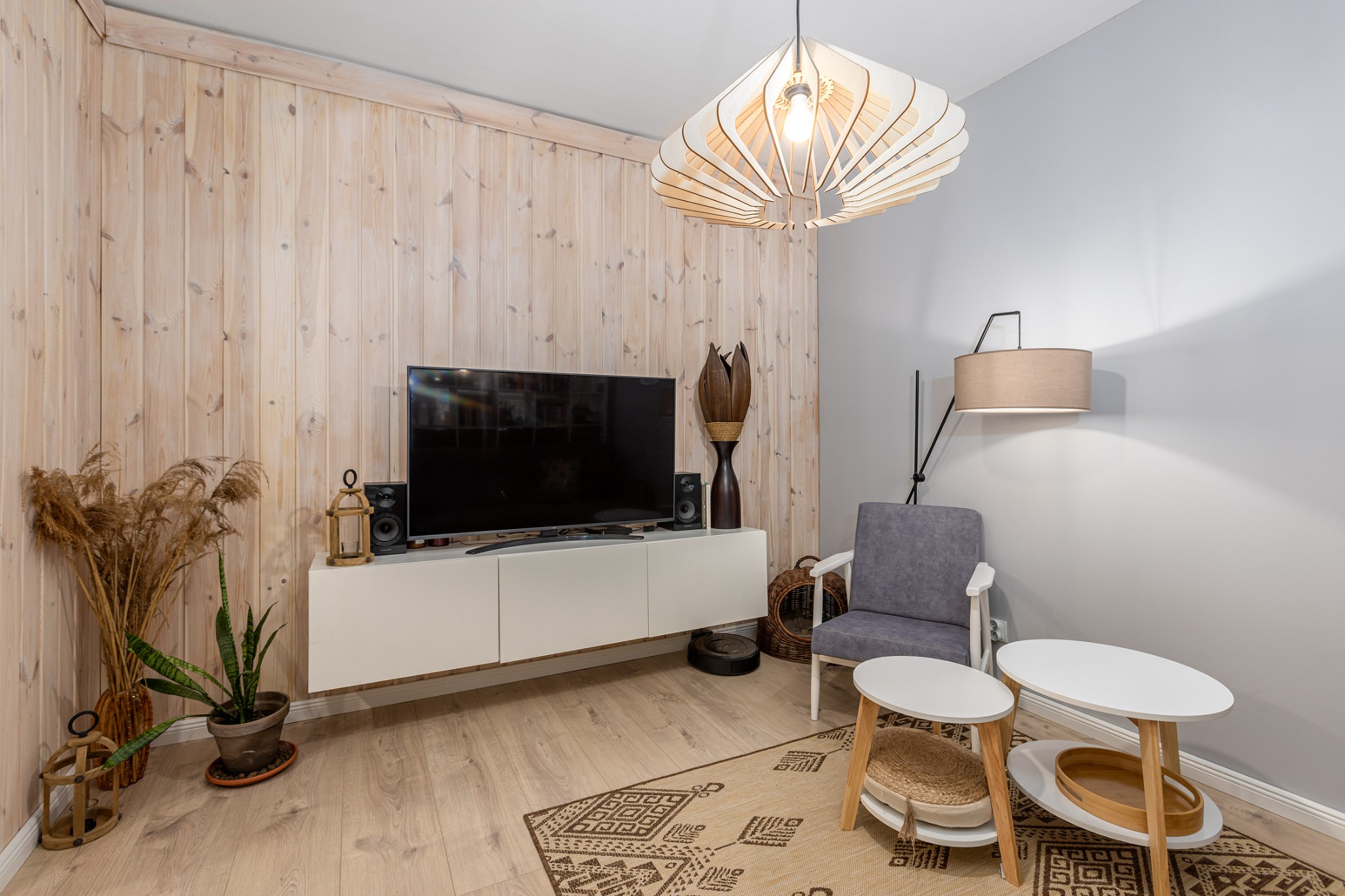 Jasne wnętrze pokoju z drewnianą boazerią, białymi meblami, szarą ścianą i dekoracjami w stylu boho.