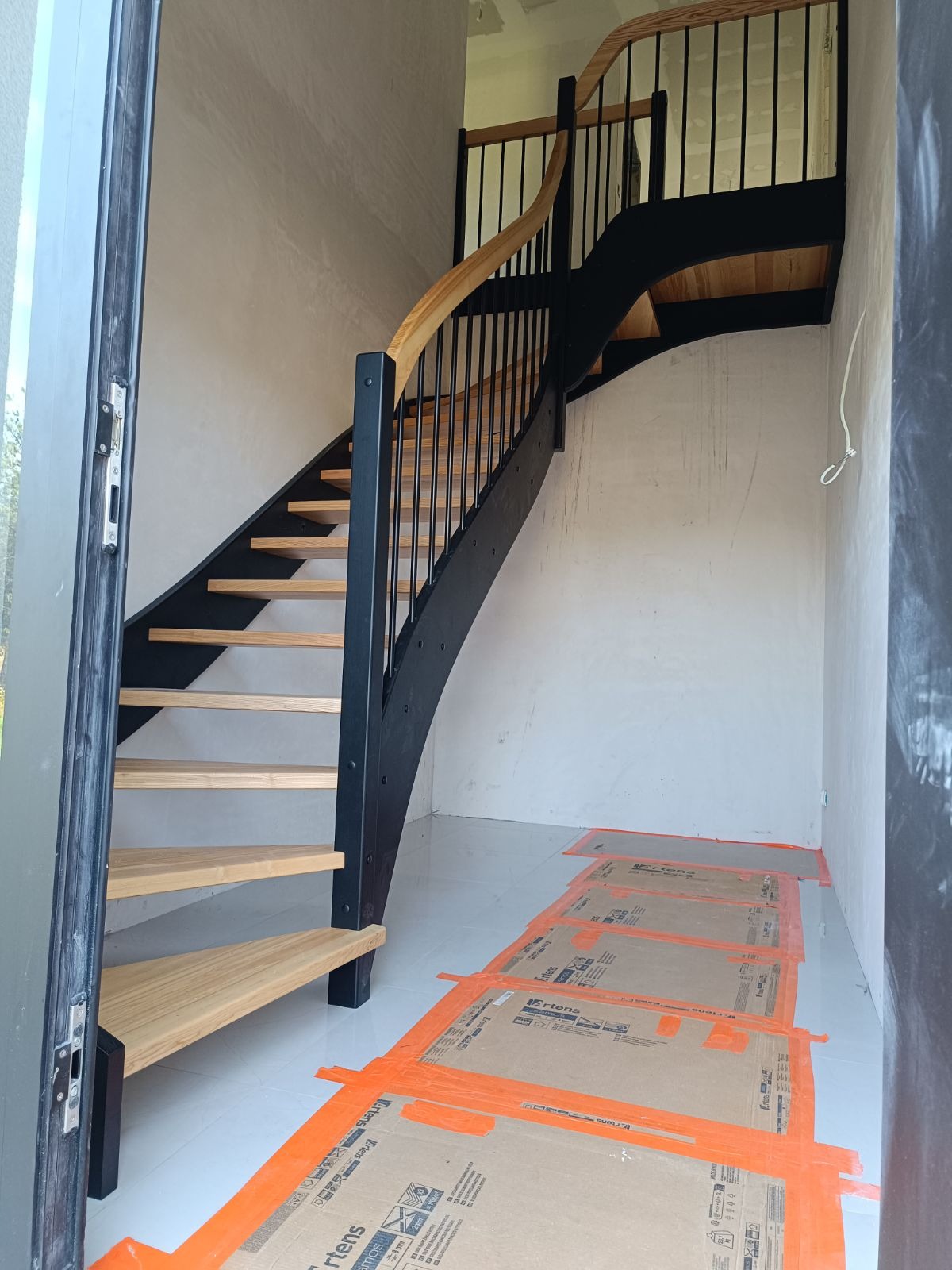Wewnętrzne schody drewniane z czarną konstrukcją i jasnymi stopniami w Samociążku, widoczne zabezpieczenia podłogi kartonem.
