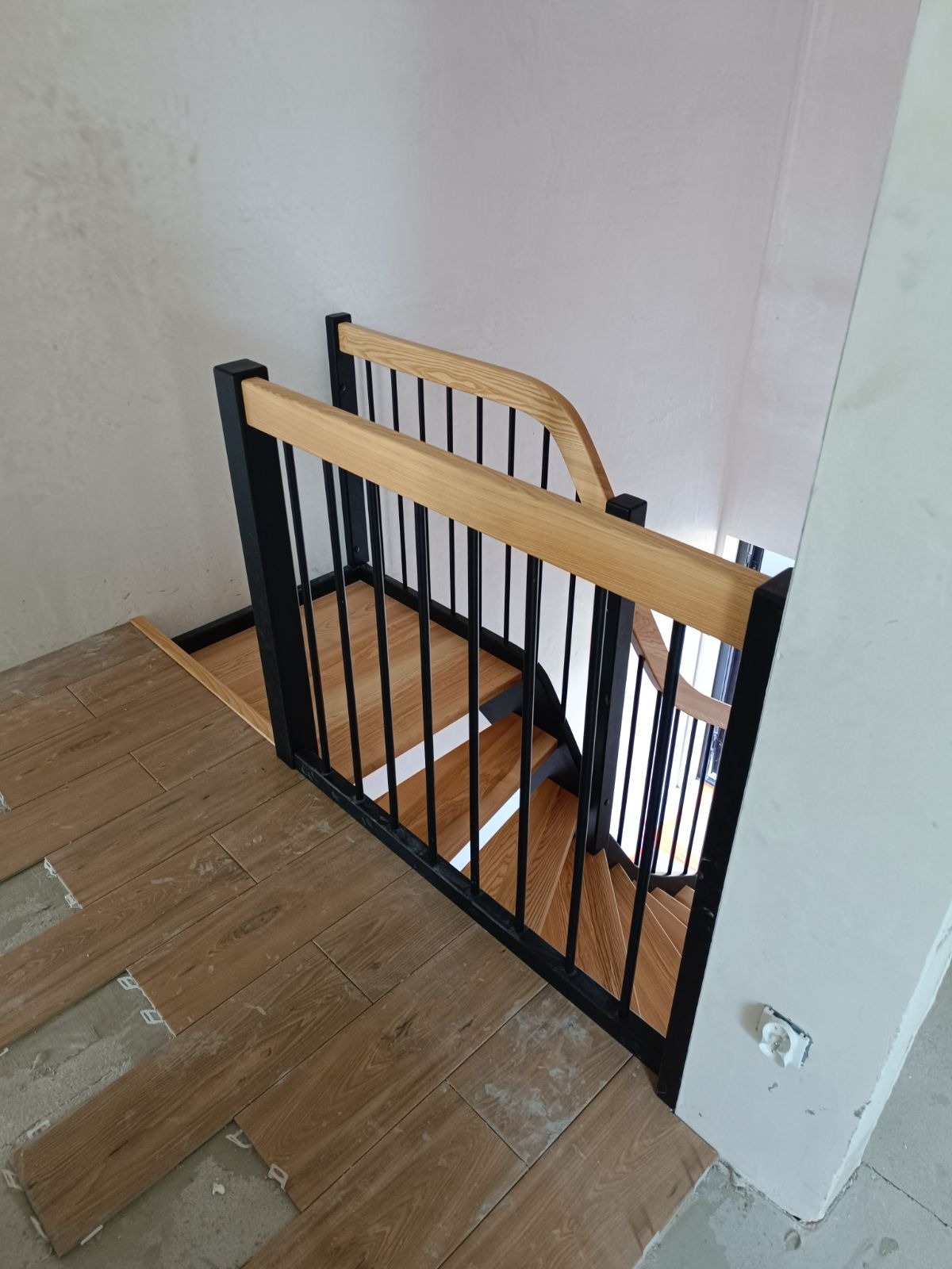Nowoczesne schody z drewnianymi stopniami i czarną metalową balustradą, widoczne podczas montażu podłogi z paneli drewnopodobnych.