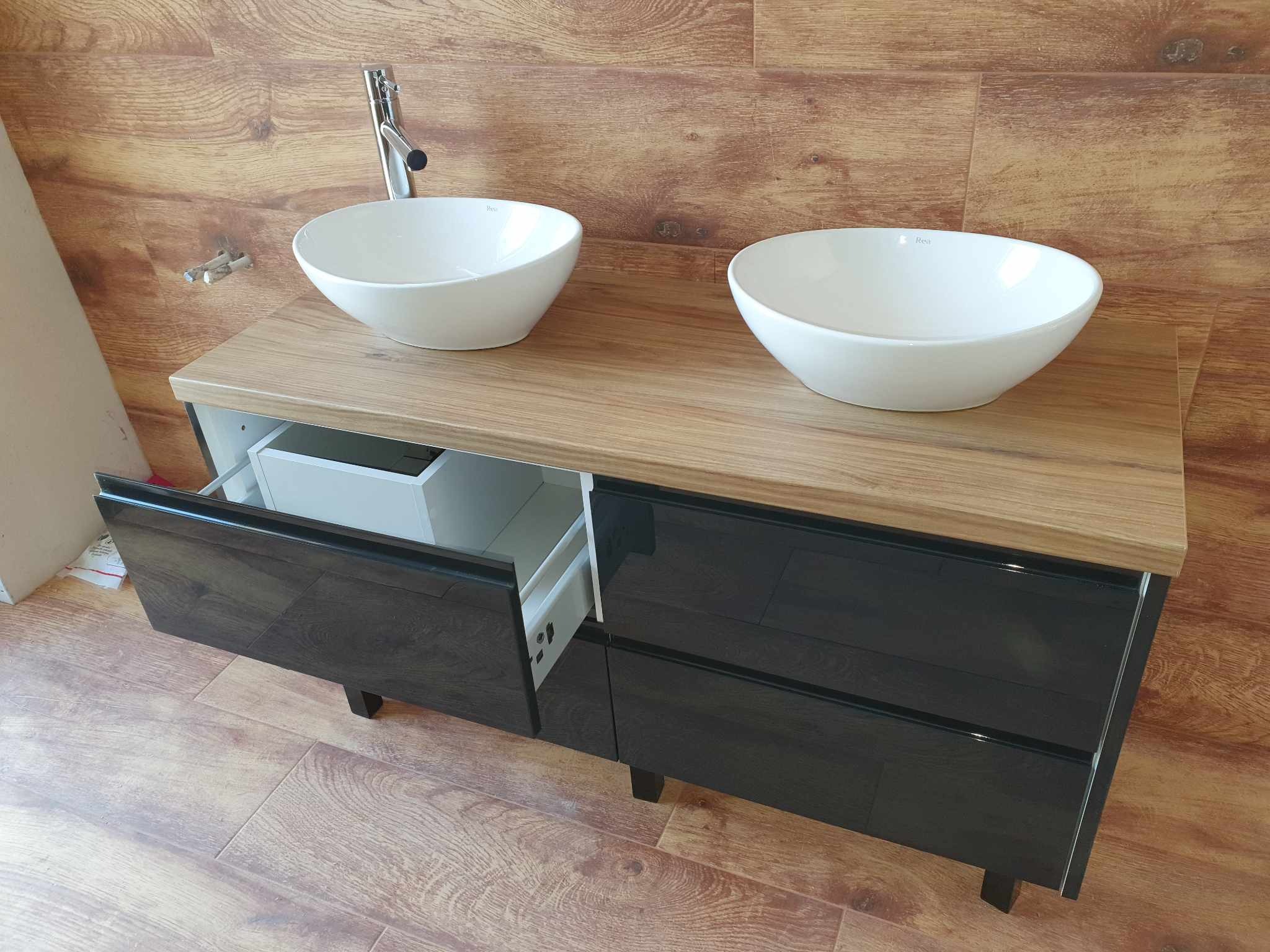 Nowoczesna szafka łazienkowa z dwoma białymi umywalkami nablatowymi, drewnianym blatem i lakierowanymi frontami szuflad w kolorze ciemnego drewna, z częściowo otwartą szufladą.