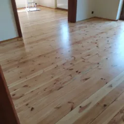 Wypolerowana drewniana podłoga z widocznym połyskiem w pomieszczeniu w Nakle nad Notecią, ze stojącą drabiną w tle i fragmentem grzejnika pod oknem.