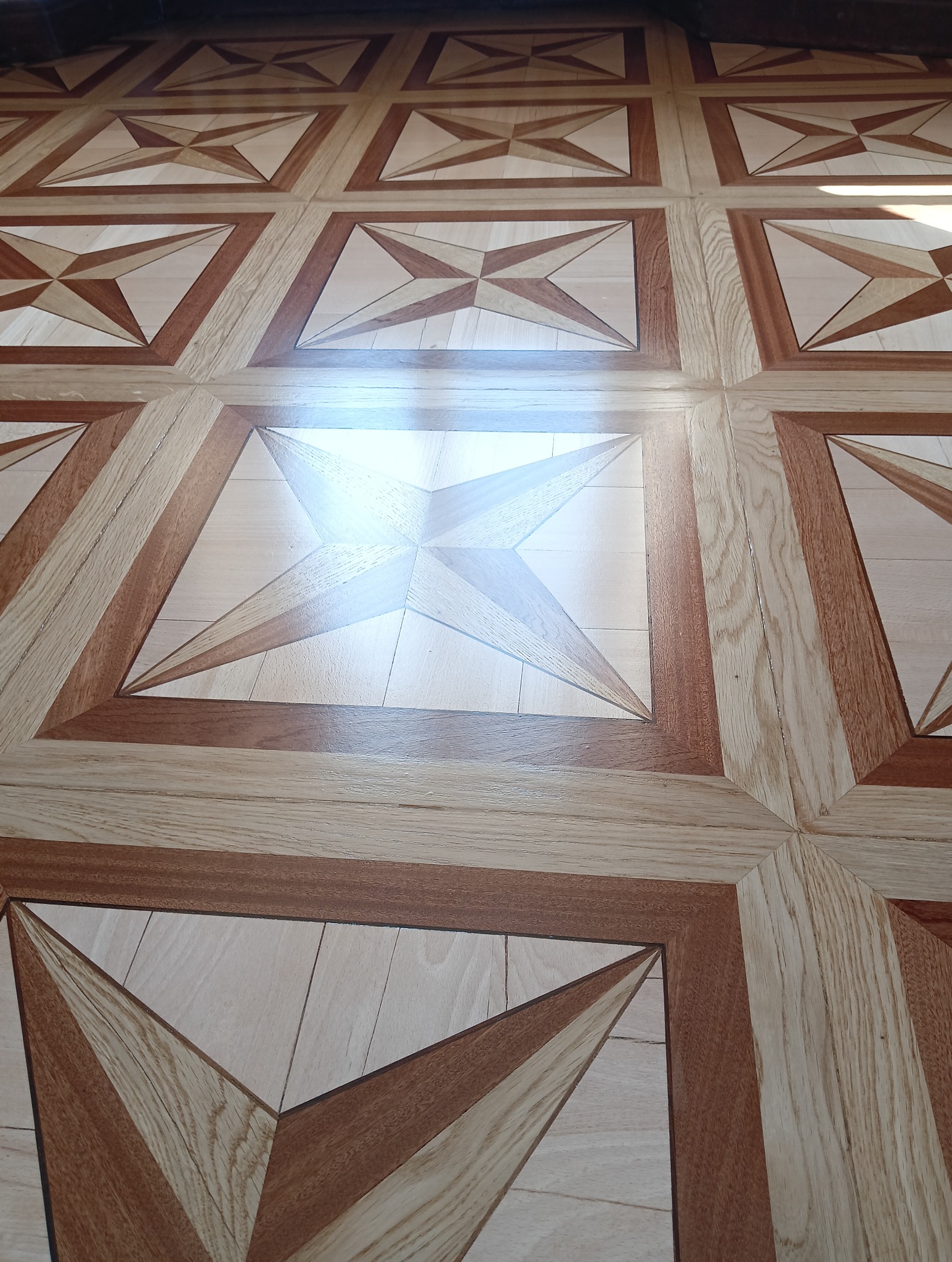 Wzór parkietu w kwadraty z motywem gwiazdy w odcieniach beżu i brązu, z refleksami światła