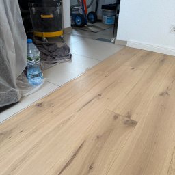 GoodWood Wilhelmus Aarts - Jasne panele podłogowe z widoczną strukturą drewna, fragment odkurzacza przemysłowego i butelka wody w tle, po zakończeniu montażu.