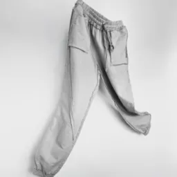 Szare spodnie dresowe z kieszeniami, wiszące na białym tle, z widocznymi surowymi wykończeniami szwów.