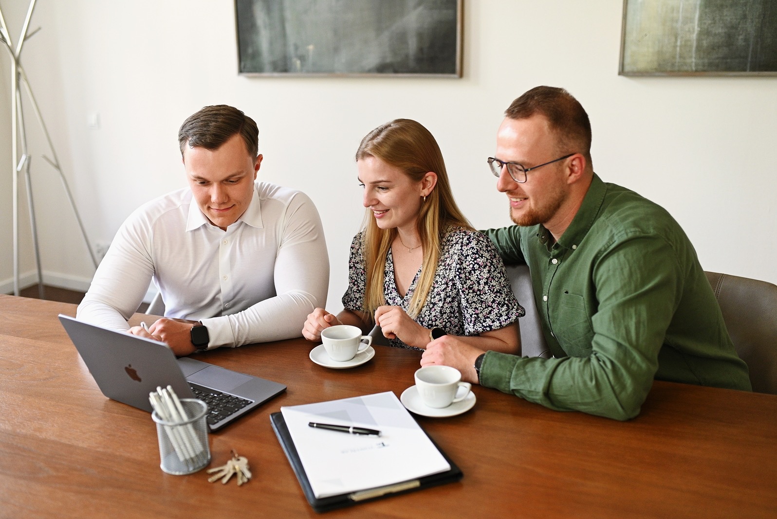 Trzech agentów nieruchomości przy drewnianym stole, omawiających ofertę na laptopie, z filiżankami kawy i dokumentami.