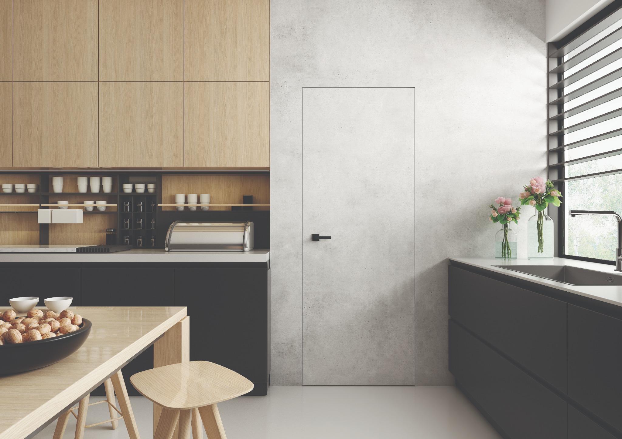 Minimalistyczna kuchnia z ukrytymi drzwiami w kolorze betonu, drewniane szafki górne, czarne szafki dolne, stół z misą orzechów i kwiaty w wazonach przy oknie.