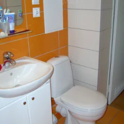 Wykończona łazienka z pomarańczowymi i białymi płytkami, umywalką z szafką i toaletą.