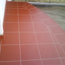 Ułożona terakota w kolorze ceglastym na zewnątrz budynku, widoczne fugi i krawędzie.