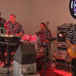 Czteroosobowy zespół w koszulach w grochy występuje na sali bankietowej, z logo 'prestige' widocznym w tle.